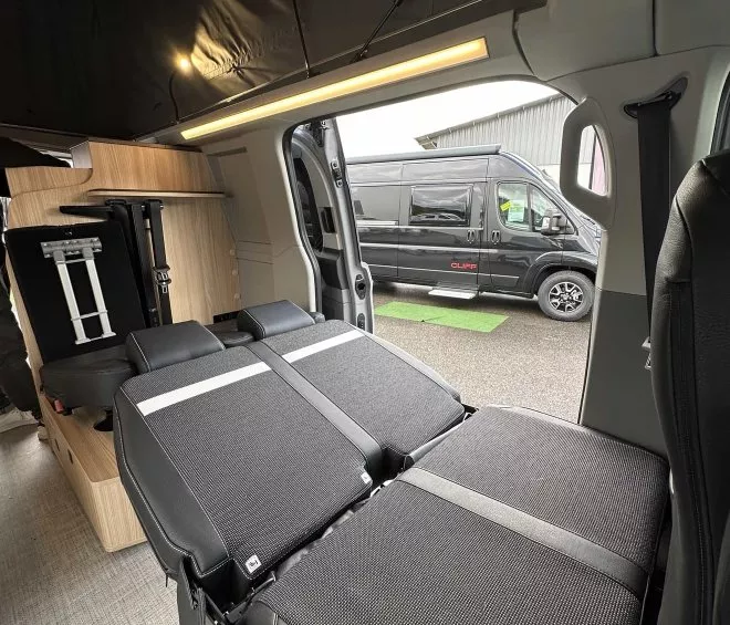 Intérieur d'un van aménagé avec banquette convertible en lit, van noir à l'extérieur.
