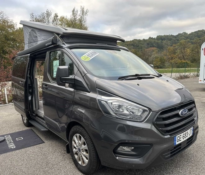 Van aménagé Ford avec toit relevable sur un parking, modèle Westfalia.