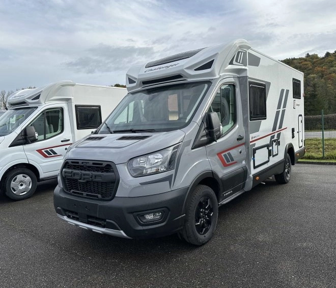 Camping-car gris stationné sur un parking, modèle moderne avec équipements extérieurs visibles.
