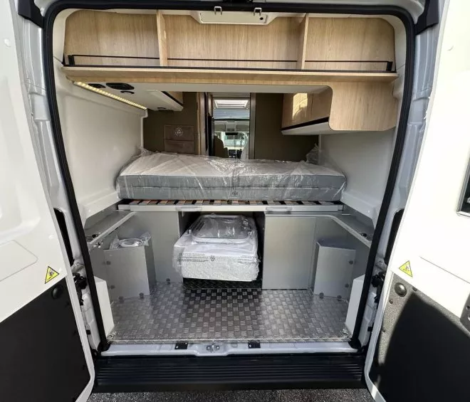 Intérieur d'un van aménagé avec lit et rangements en bois clair.