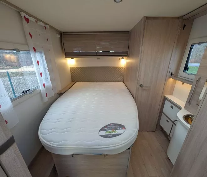 Intérieur d'une caravane avec lit double, rangements en bois et rideaux à motifs cœurs.