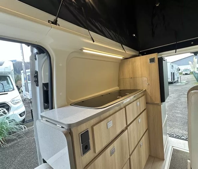 Intérieur d'un van aménagé avec cuisine en bois clair et éclairage LED.
