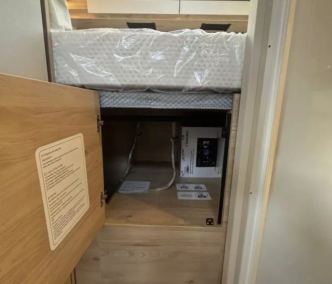 Intérieur d'un camping-car avec lit surélevé et espace de rangement en bois.