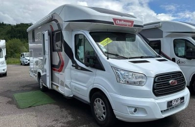 Camping-car Challenger blanc stationné sur un parking, ciel nuageux en arrière-plan.