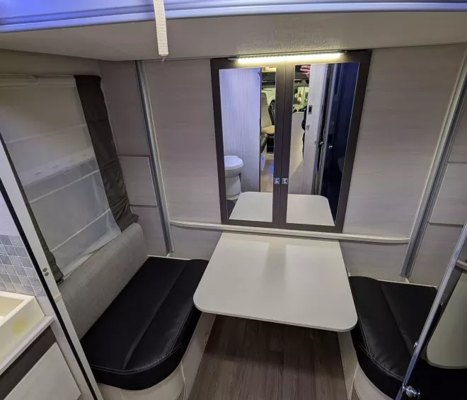 Intérieur d'une caravane avec coin repas, table pliante et banquettes noires