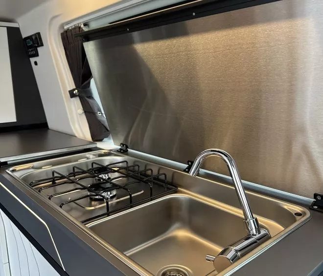 Cuisine compacte avec évier et plaque de cuisson intégrés dans un véhicule aménagé.