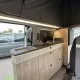 Intérieur d'un van aménagé avec cuisine moderne et espace de rangement en bois clair.