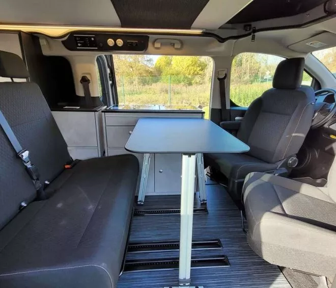 Intérieur d'un van aménagé avec table et sièges, vue sur l'extérieur