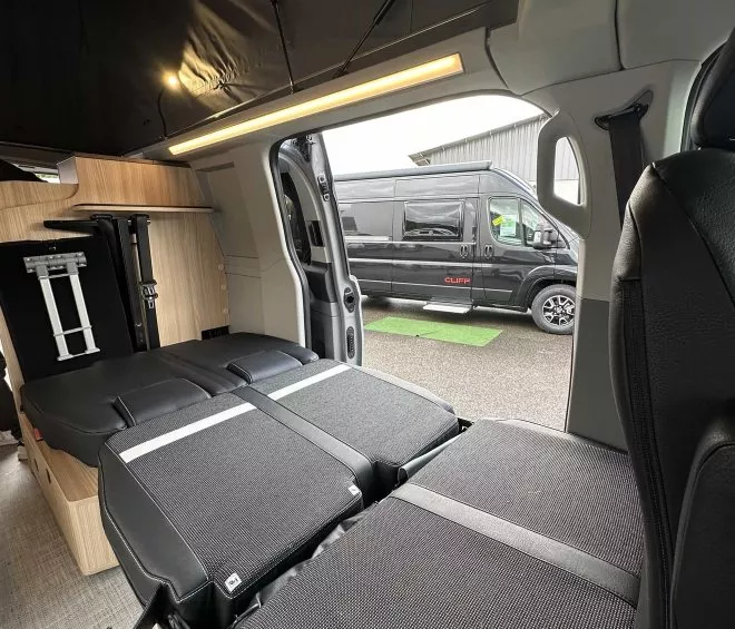 Intérieur d'un van aménagé avec lit déplié, van noir à l'extérieur