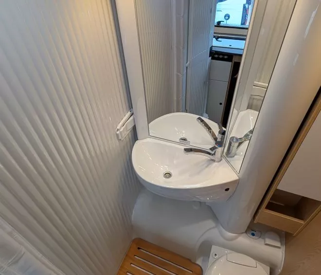Salle de bain compacte avec lavabo, miroir et toilettes dans un camping-car moderne.