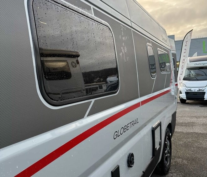 Camping-car Globetrail stationné sur un parking, ciel nuageux en arrière-plan.