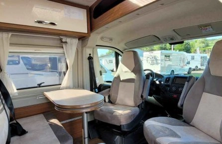 Intérieur d'un camping-car avec sièges et table, vue sur l'extérieur.
