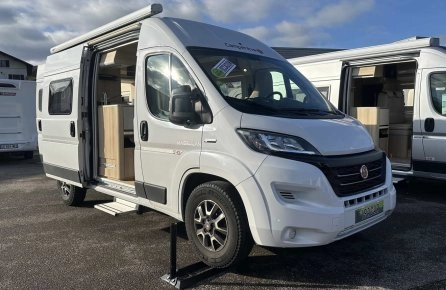 Camping-car blanc stationné avec porte ouverte, ciel nuageux