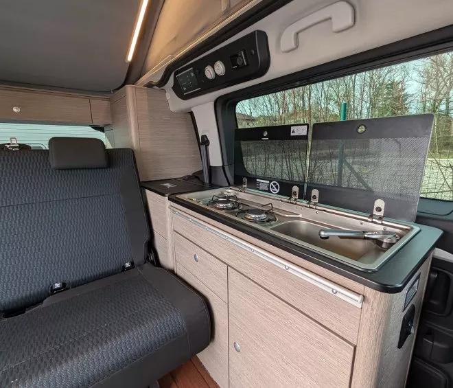 Intérieur d'un van aménagé avec cuisine et sièges en tissu noir.
