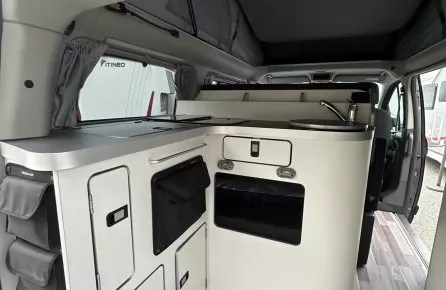 Intérieur d'un van aménagé avec cuisine compacte et rangements intégrés.