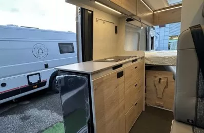 Intérieur moderne d'un camping-car avec cuisine équipée et rangements en bois clair.