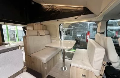 Intérieur d'un van aménagé avec sièges et table en bois clair, éclairage LED