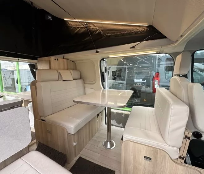 Intérieur d'un van aménagé avec sièges et table en bois clair, éclairage LED