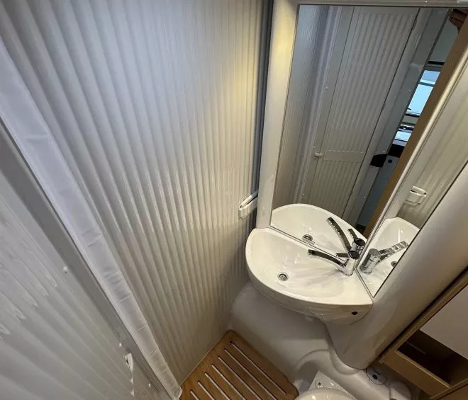 Salle de bain compacte avec lavabo, toilettes et sol en bois dans un camping-car.