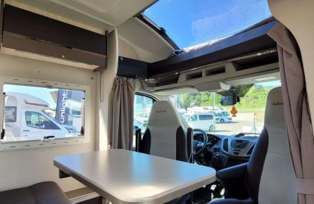 Intérieur d'un camping-car avec table et sièges, vue sur l'extérieur ensoleillé
