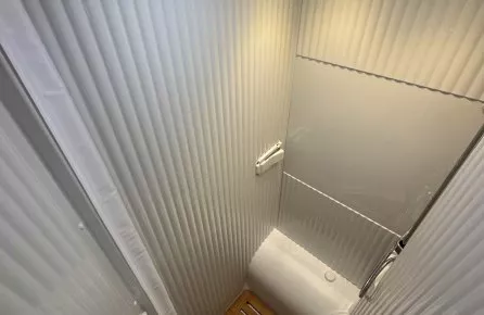 Douche compacte avec parois blanches et sol en bois, éclairage intégré, vue depuis le haut.