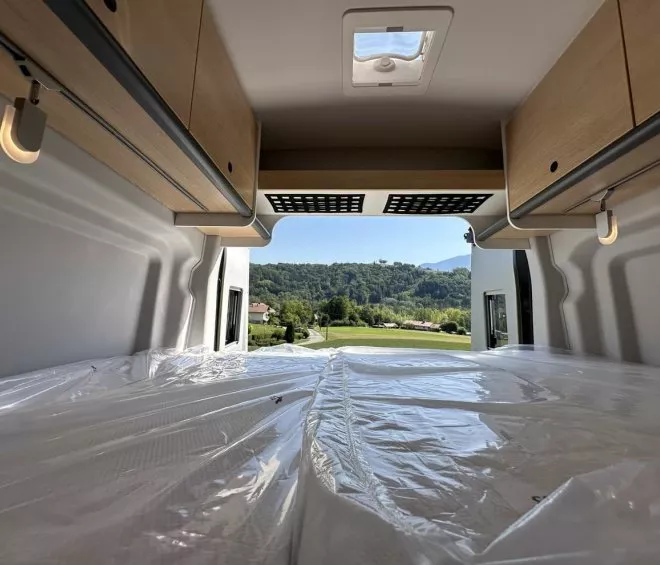 Intérieur d'un van aménagé avec vue sur la campagne verdoyante par la porte arrière ouverte.