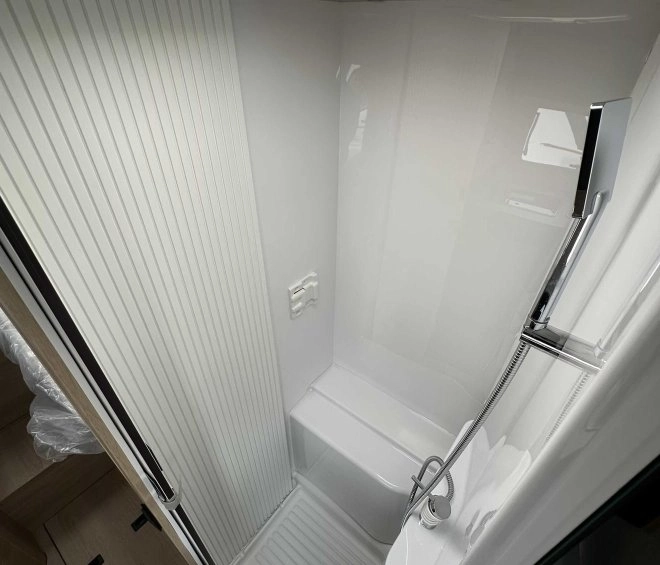 Douche compacte avec parois blanches et pommeau, dans un espace restreint de véhicule récréatif.