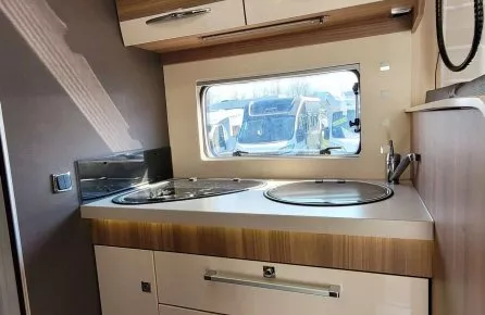 Cuisine compacte de camping-car avec placards en bois et fenêtre.