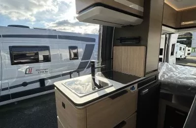 Intérieur d'un camping-car moderne avec cuisine équipée et vue sur un autre véhicule stationné.