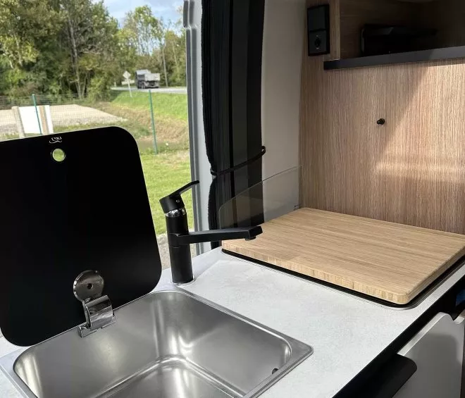 Évier en acier inoxydable dans une kitchenette de camping-car moderne avec planche à découper en bois.