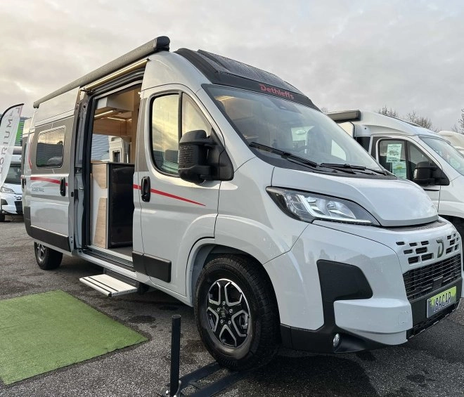 Camping-car Dethleffs blanc avec porte latérale ouverte sur un parking.