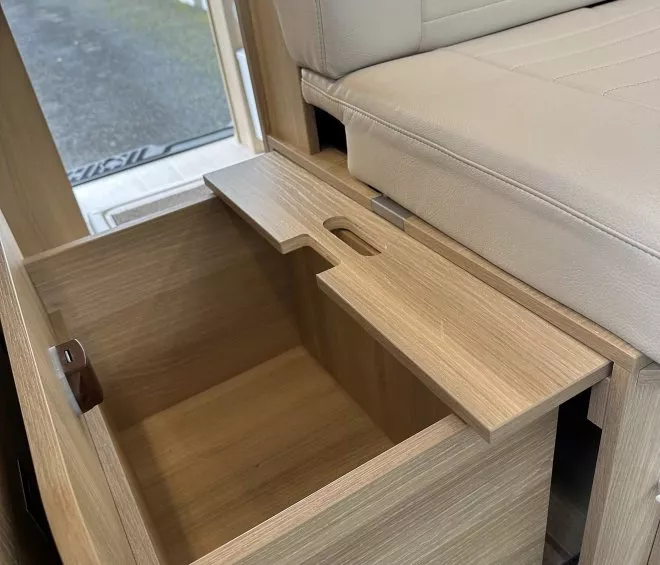 Rangement en bois sous un siège beige dans un véhicule aménagé