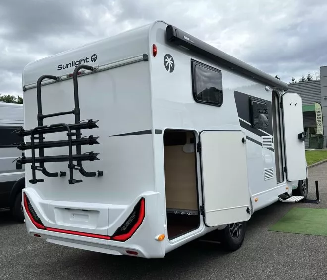 Camping-car Sunlight avec porte ouverte et porte-vélos arrière sur un parking.