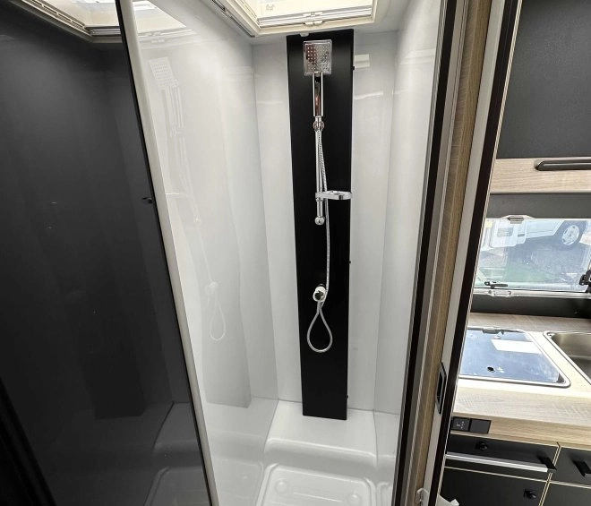 Douche moderne dans un camping-car avec puits de lumière et parois vitrées.