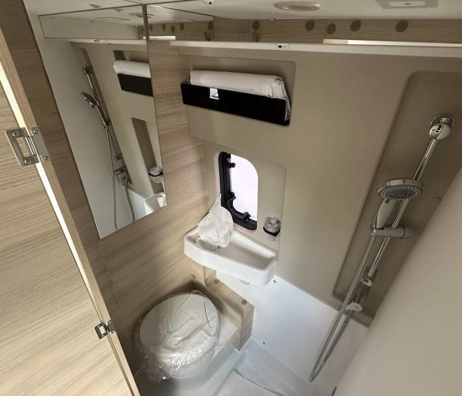Salle de bain compacte avec douche, lavabo et toilettes dans un camping-car moderne.