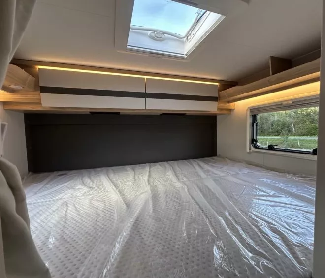 Intérieur d'un camping-car avec lit double, rangement et fenêtre ouverte sur la nature.