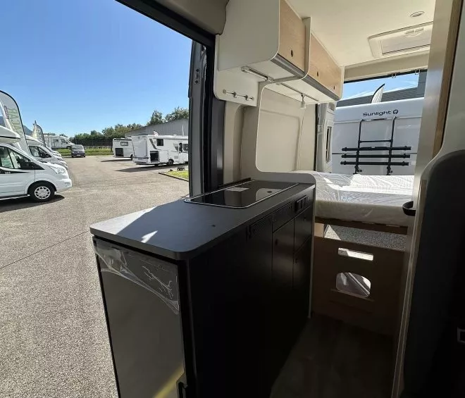 Intérieur d'un camping-car avec cuisine équipée et espace de rangement, stationné sur un parking.
