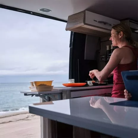 Personne cuisinant dans un van aménagé face à la mer
