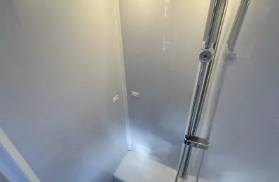 Douche moderne avec parois blanches et éclairage intégré, équipée d'une colonne de douche chromée.