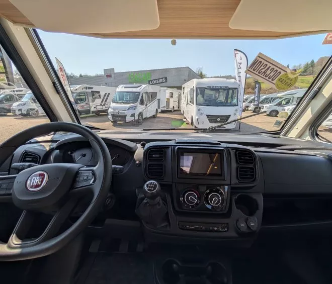 Vue intérieure d'un camping-car Fiat avec d'autres véhicules en exposition chez Isacar Loisirs.
