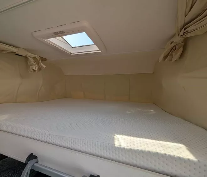 Espace couchage avec matelas et hublot dans un camping-car moderne