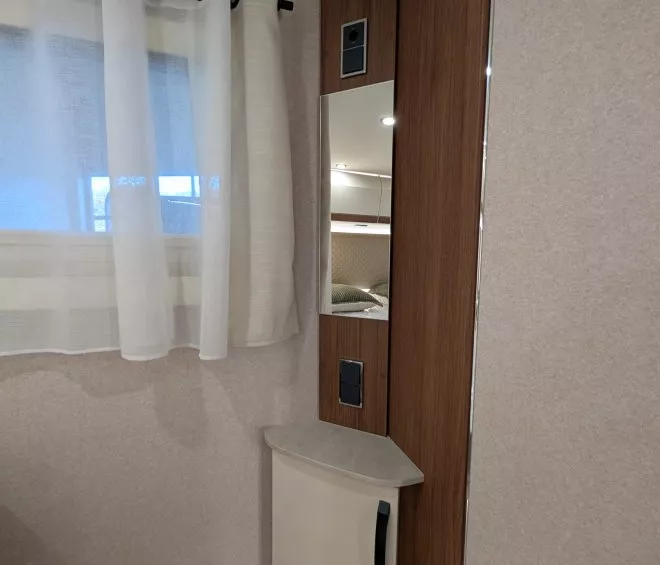 Coin intérieur de caravane avec rideau blanc et meuble en bois clair