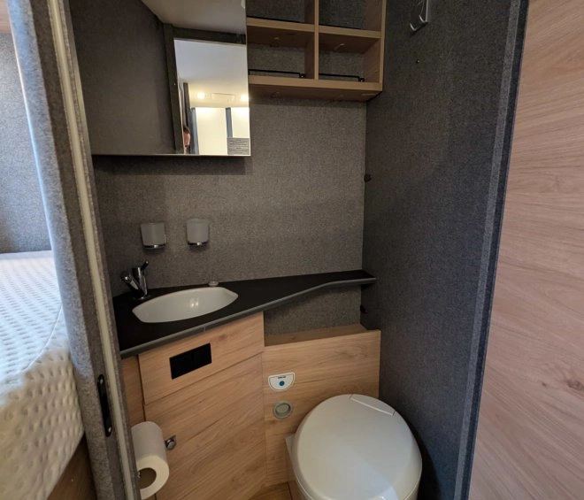 Salle de bain compacte avec lavabo, toilettes et rangements en bois dans un camping-car.