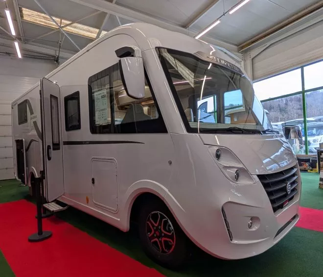 Camping-car blanc exposé dans un showroom lumineux avec sol rouge et vert.
