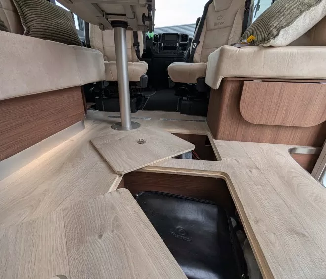 Intérieur d'un camping-car avec rangement au sol ouvert et sièges en cuir beige.