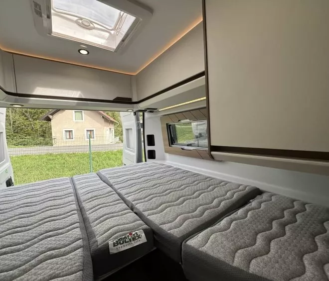 Intérieur d'un van aménagé avec lit double et vue extérieure sur jardin
