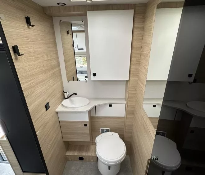 Salle de bain moderne avec lavabo, toilettes et placards en bois clair dans un camping-car.