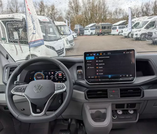 Intérieur d'un véhicule Volkswagen avec écran de contrôle, vue sur camping-cars en arrière-plan.
