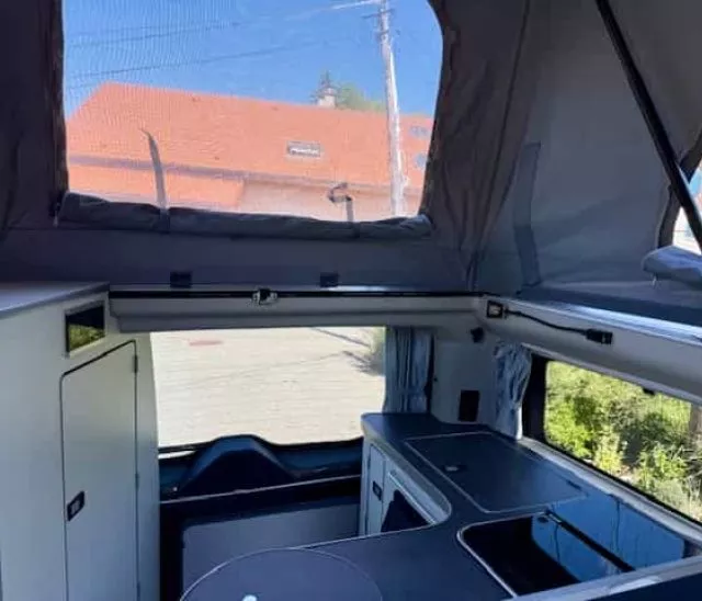 Intérieur d'un van aménagé avec toit relevable et cuisine intégrée.