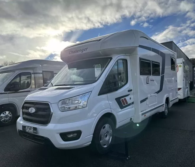 Camping-car Challenger blanc stationné sur un parking sous un ciel nuageux